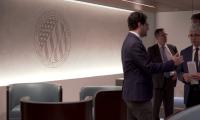 Men in suits talking in front of the logo of the FEC on the wall
