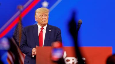 Donald Trump standing on a stage beside a podium with silhouettes of hands from a crowd in front of him