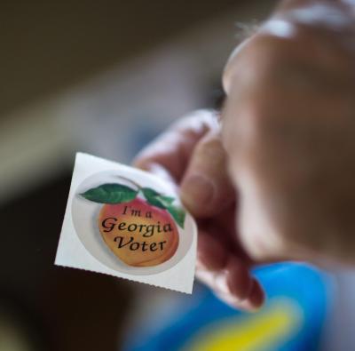 Hands holding a sticker with a peach on it that says "I'm a Georgia Voter"
