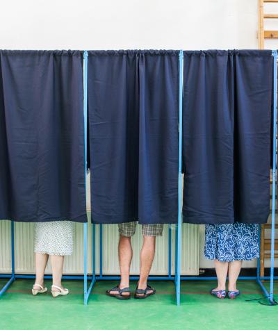 People in voting booths with only their feet visible beneath the curtains