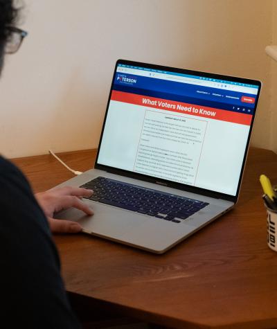 A man sitting at a laptop viewing a website with a banner that says "What Voters Need to Know"